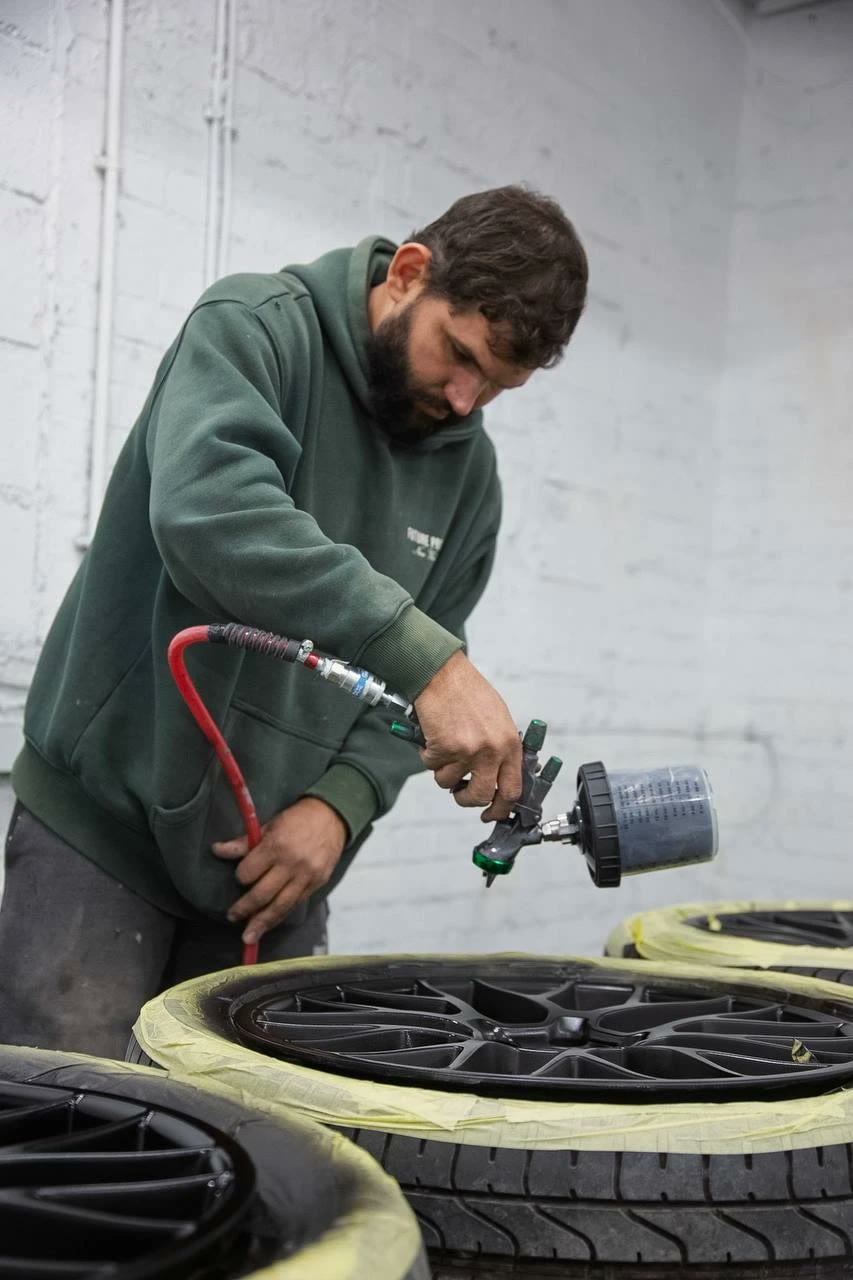 Technician spraying a set of masked alloy wheels in gloss black