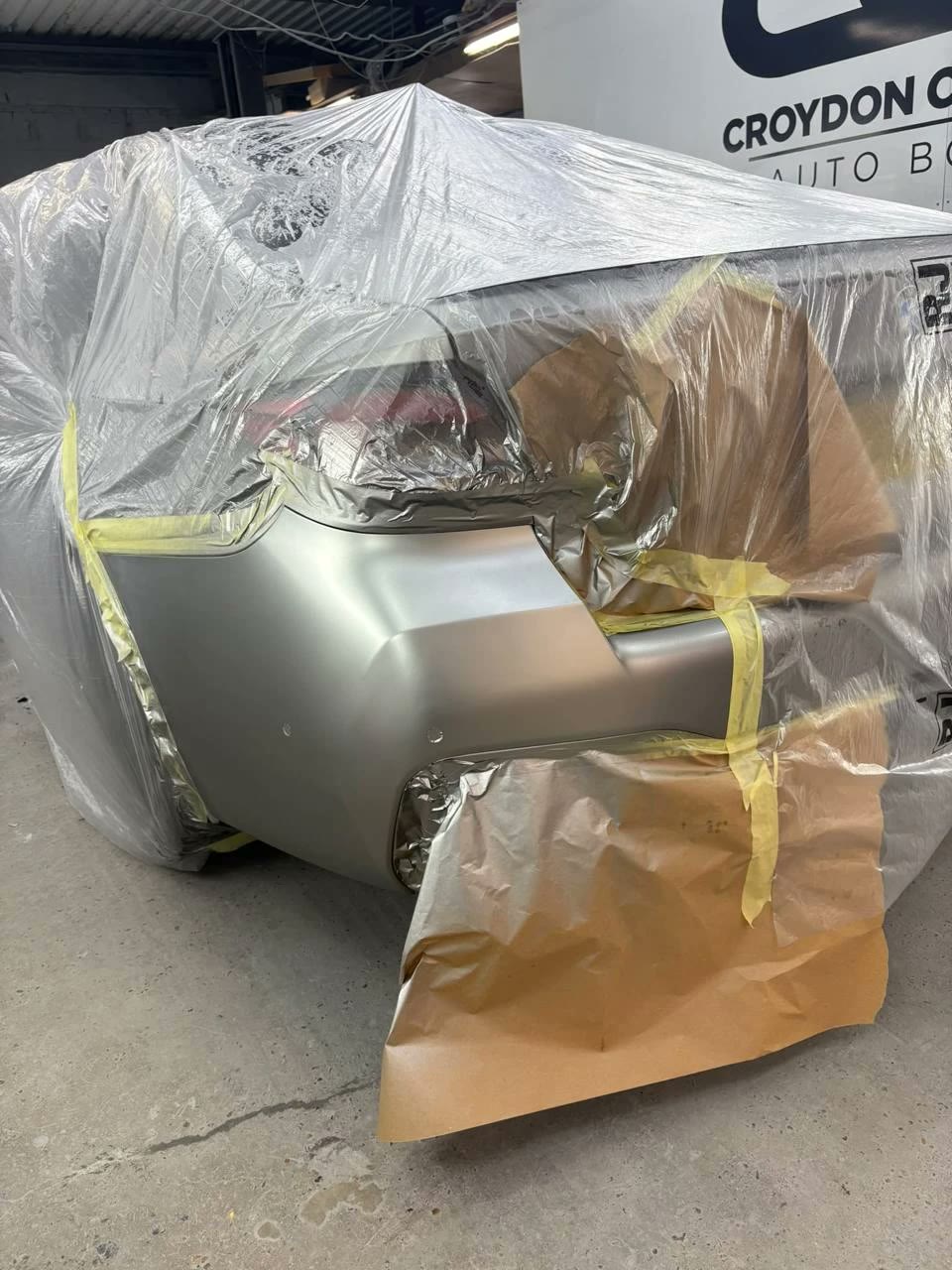 Silver rear bumper freshly painted in the Croydon Coach Works booth with the rest of the car masked off
