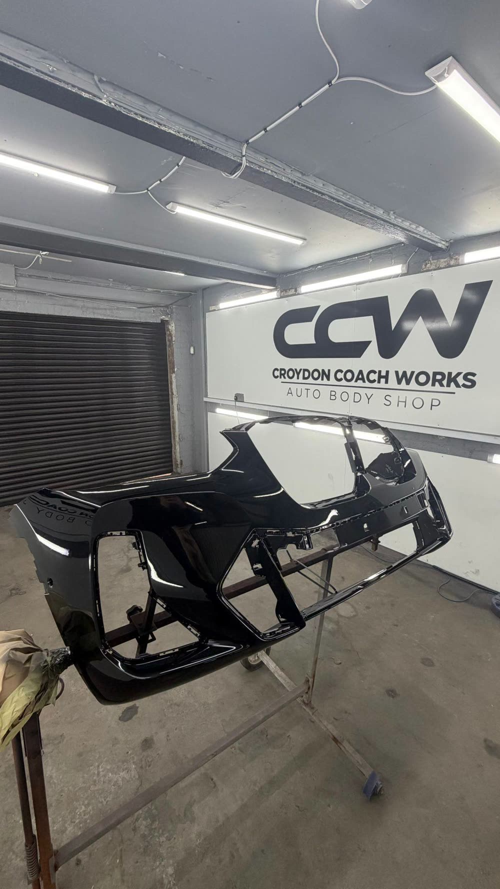 Front bumper painted gloss black on a stand in front of the Croydon Coach Works sign
